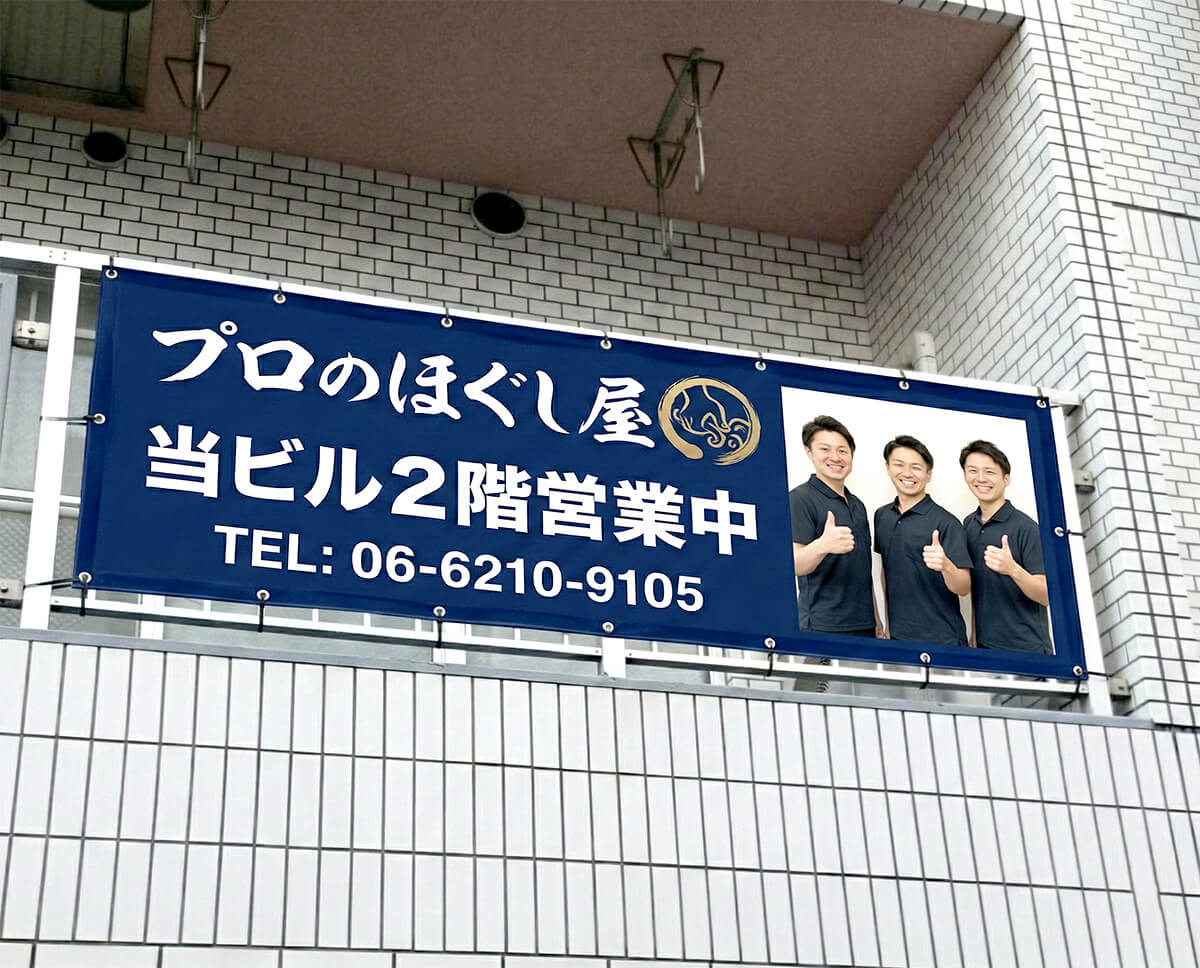 もみほぐし専門店プロのほぐし屋の店頭幕施工完成写真｜スタッフ写真入りネイビー横断幕完成