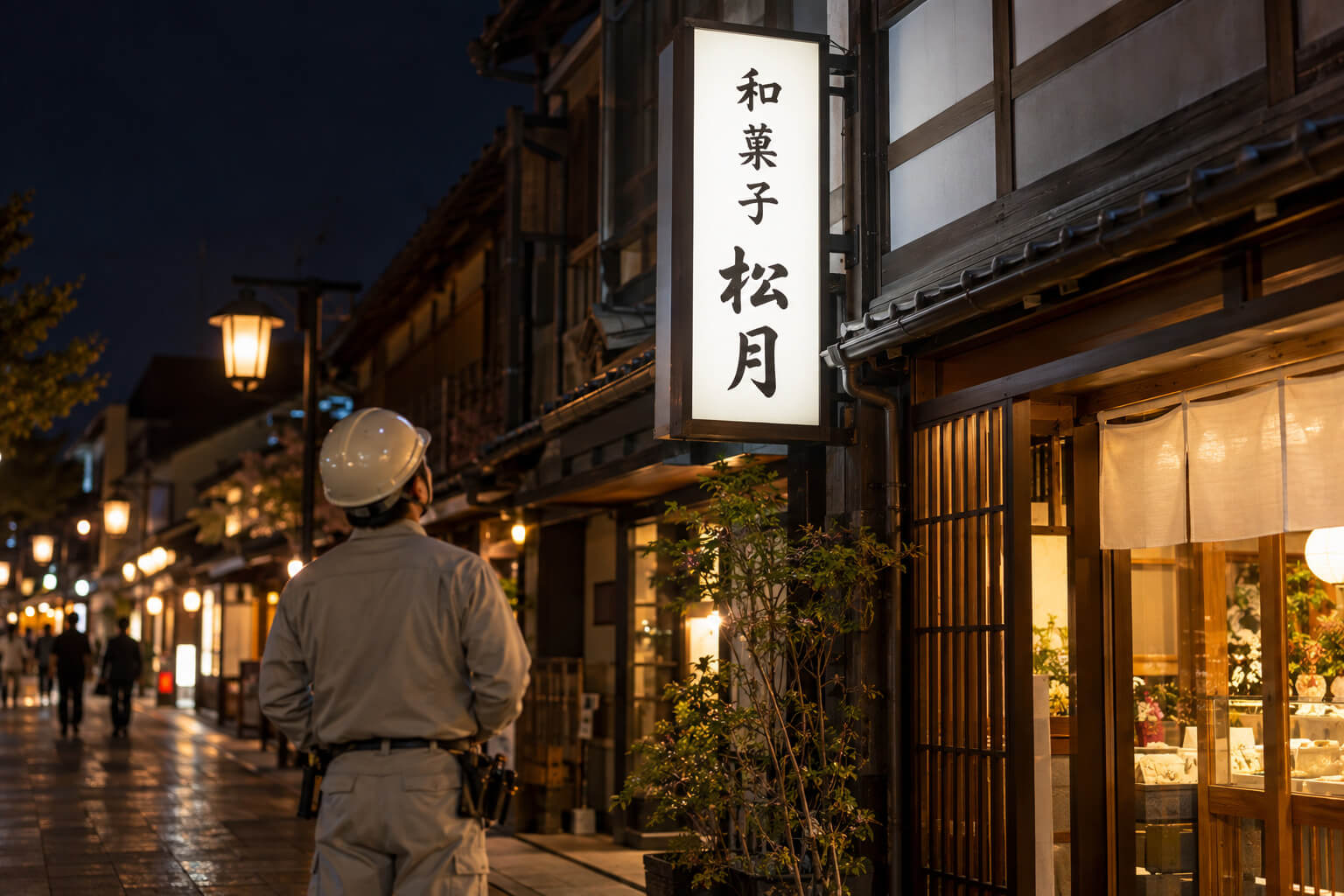 修理を終えて明るく点灯した袖看板を、職人が夜に見上げて確認している様子