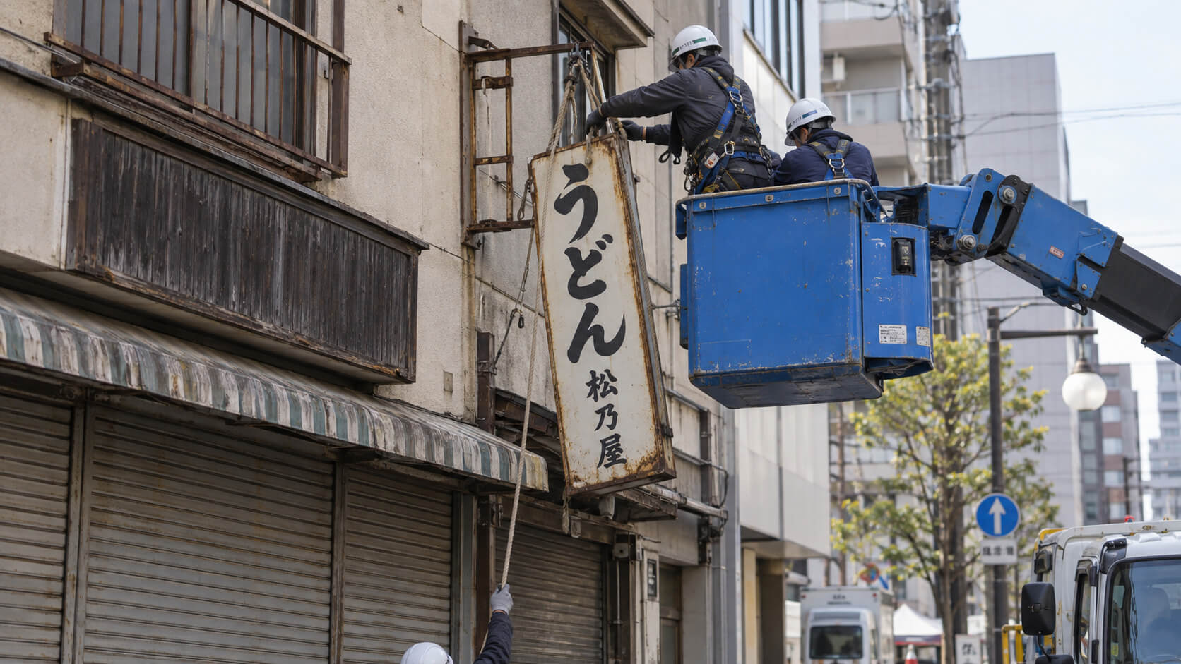 高所作業車を使ってビル2階の袖看板を取り外している職人