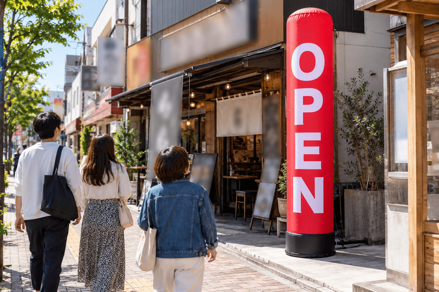 ラーメン店の入口の横の敷地に、赤と黄色で「らーめん」と大きく書かれた全高3mのエアー看板が立っている昼の様子