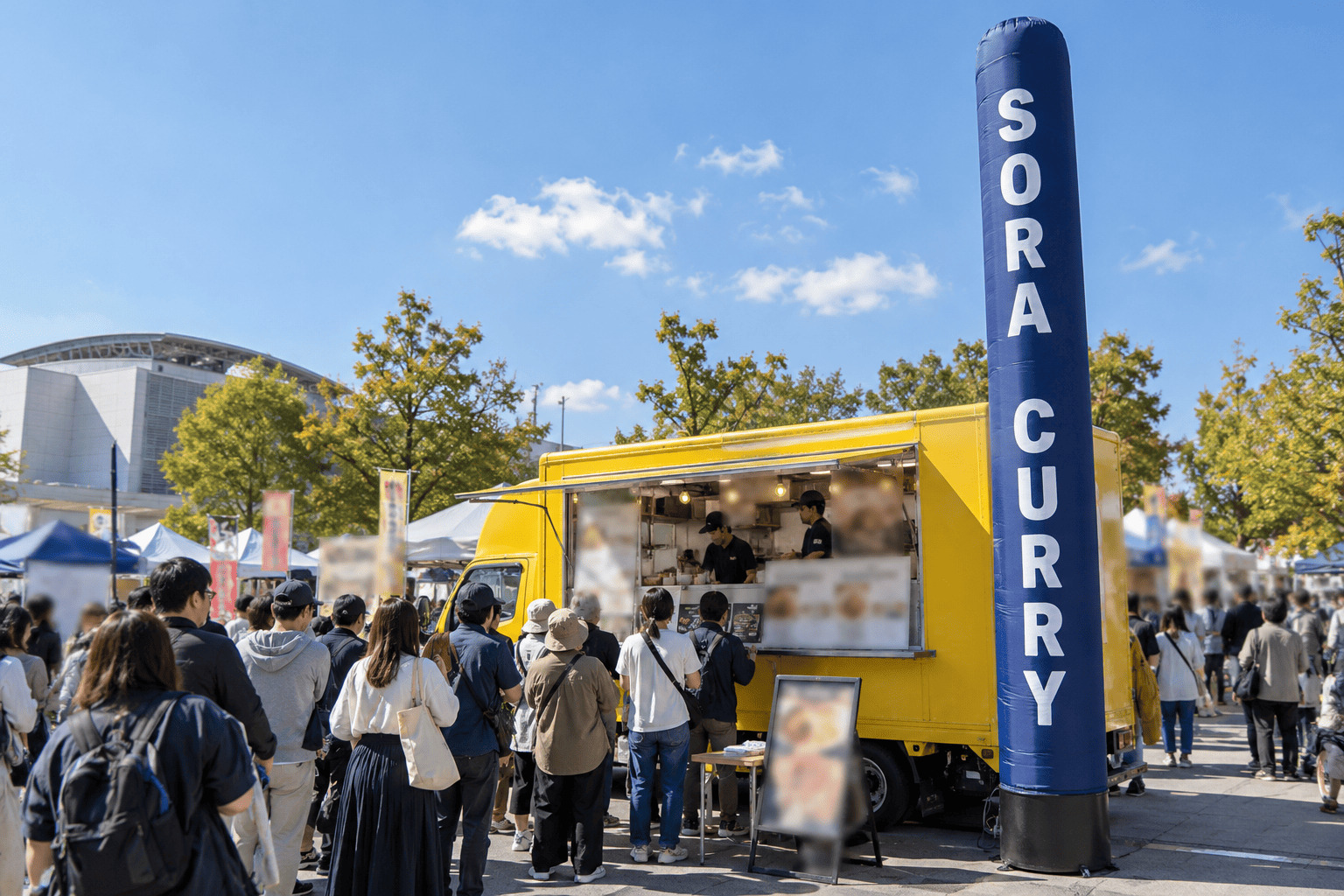 イベント会場に止めたキッチンカーの横に、店名の入った全高5mの細長いエアー看板が立ち、人だかりの上に看板が見えている様子