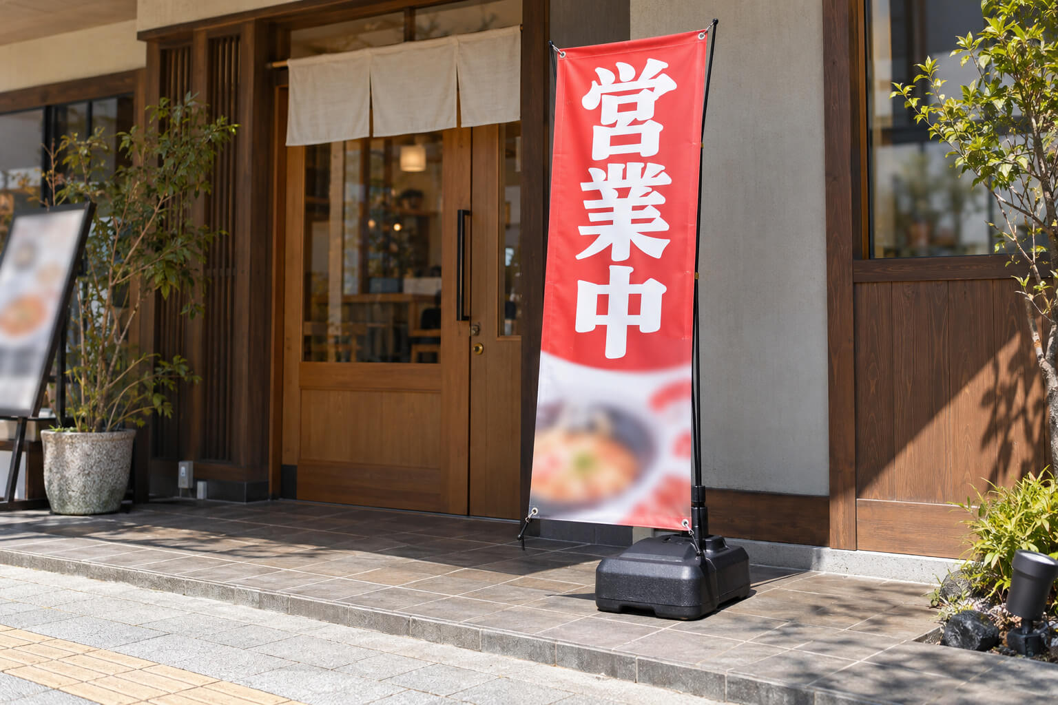 飲食店の店先の敷地内に、注水タンク付きのXバナーが立っている様子