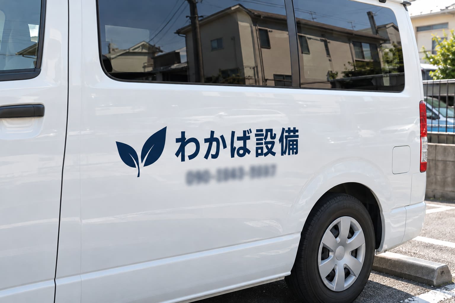 白いワンボックス車の側面に、紺色のカッティングシートの社名とロゴ、電話番号が貼られている様子