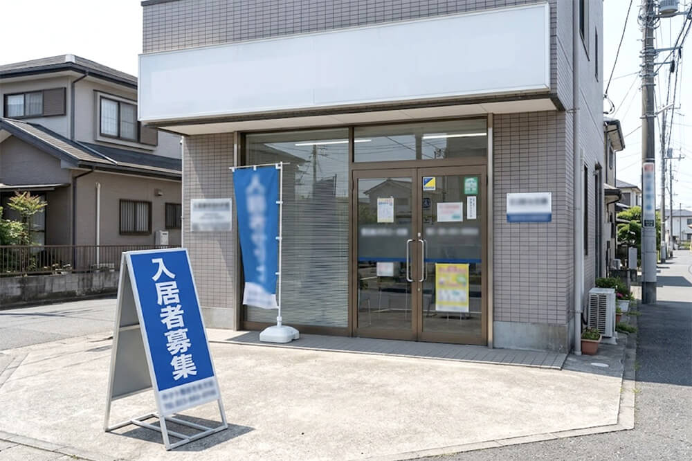 不動産会社の店先に、「入居者募集」の折りたたみ看板と、のぼり、プレート看板が並べて置かれている様子