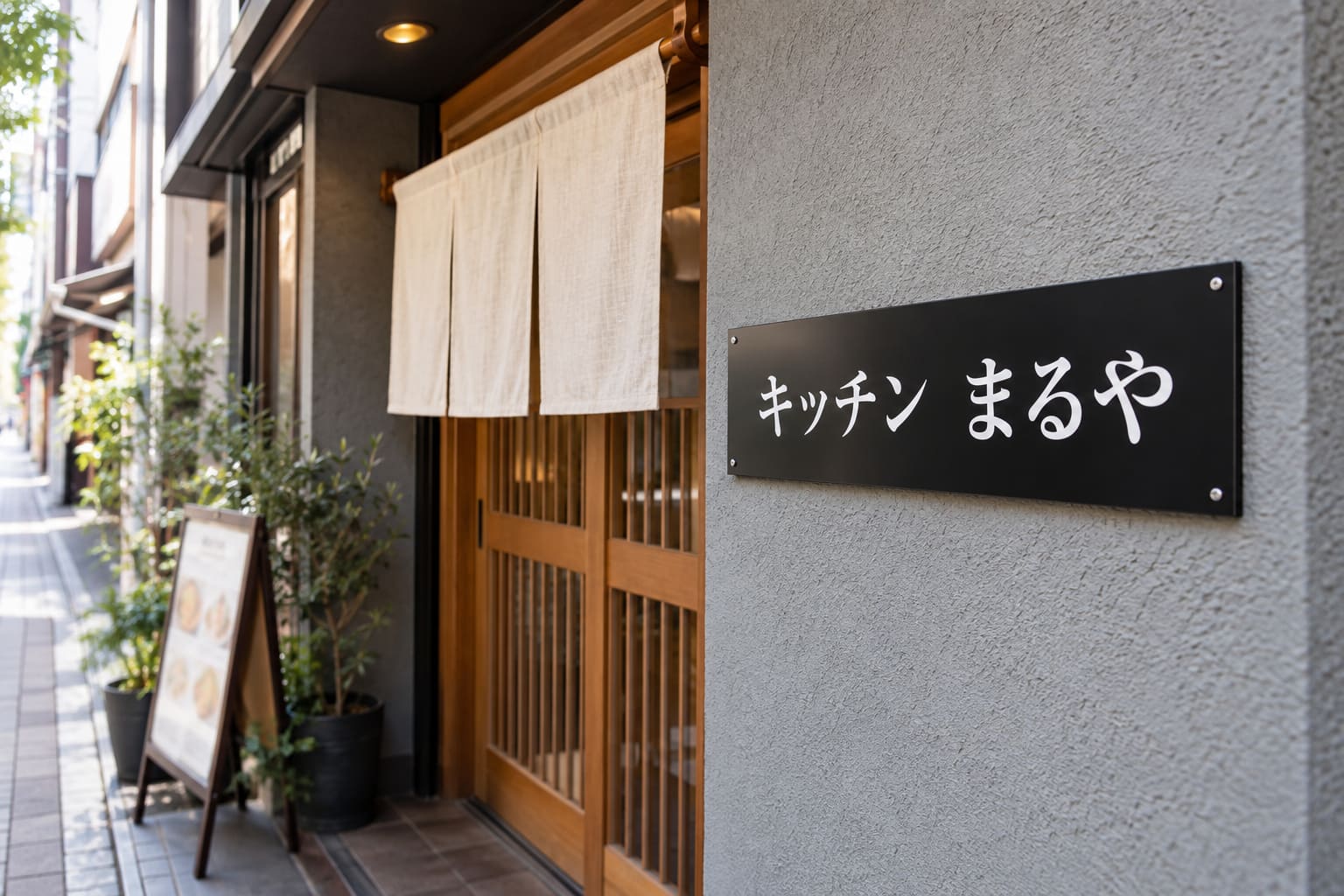 飲食店の入口の横の壁に、店名を印刷した横長の平看板が取り付けられている様子