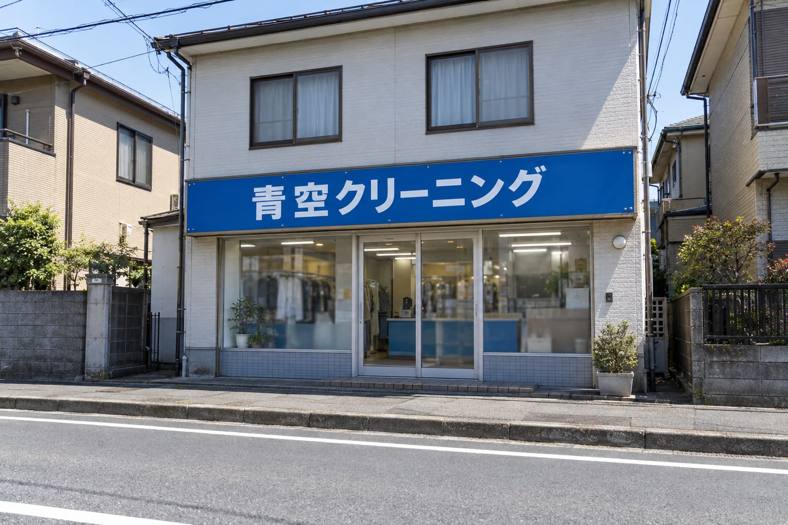 道路の向こう側の歩道から見た、2階建ての店舗の1階の壁に付いた横長の平看板