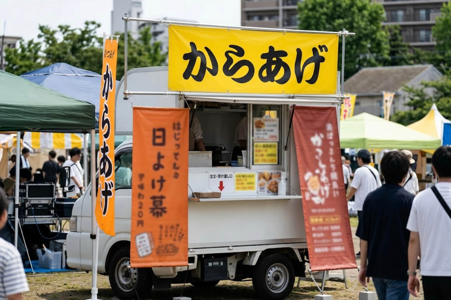 キッチンカーの販売口の上と横に、メニューと店名を印刷した幕が取り付けられている様子