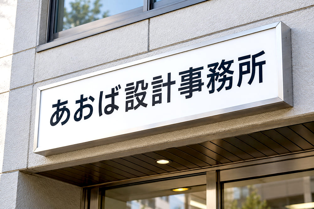 事務所の入口の上の外壁に、シルバーのアルミ枠で縁取られた社名のプレート看板が付いている様子