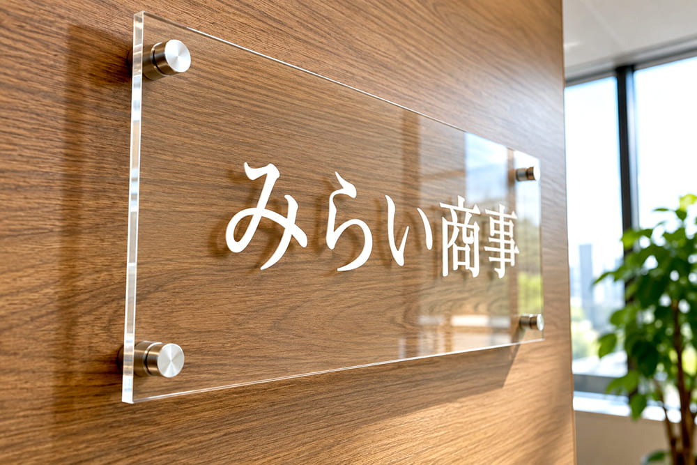 受付の壁に、木目の板の手前に透明のアクリル板を重ねた二重構造の社名看板が付いている様子を斜めから見たところ