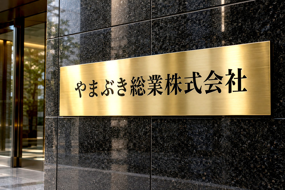 本社ビルの入口の黒い石の壁に、金色のステンレス板に黒い文字で会社名が入ったエッチング銘板が付いている様子