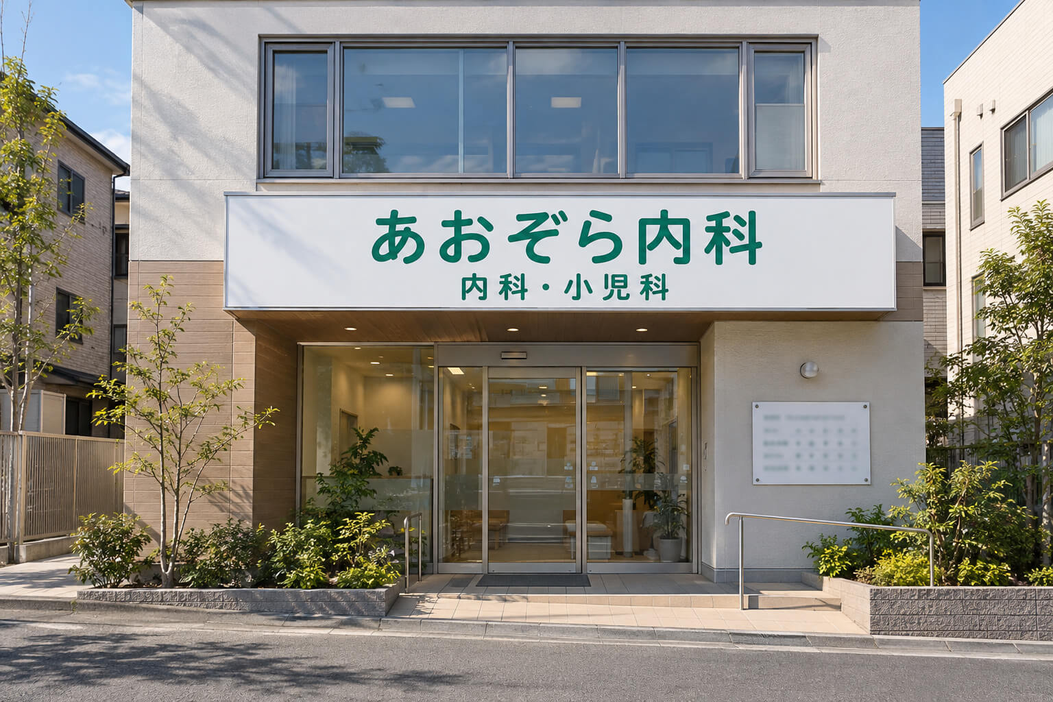 2階建てのクリニックの正面に、白地に緑の文字で医院名と診療科目が入った横長の看板があり、入口の横に小さな診療時間の案内板がある様子