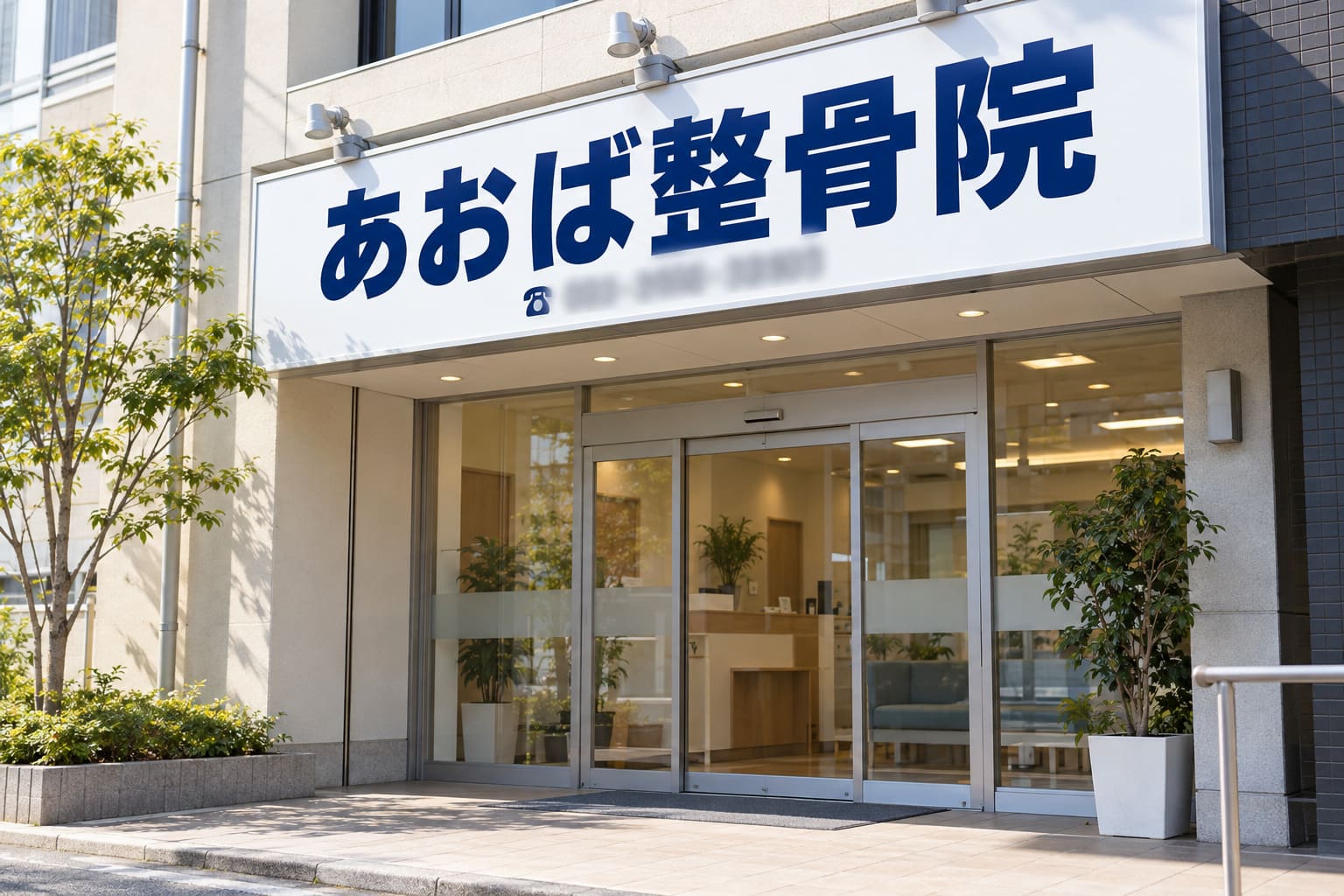 白い壁面看板に、紺色の太い角ゴシック体で「あおば整骨院」と大きく書かれ、下に電話番号が入った整骨院の外観
