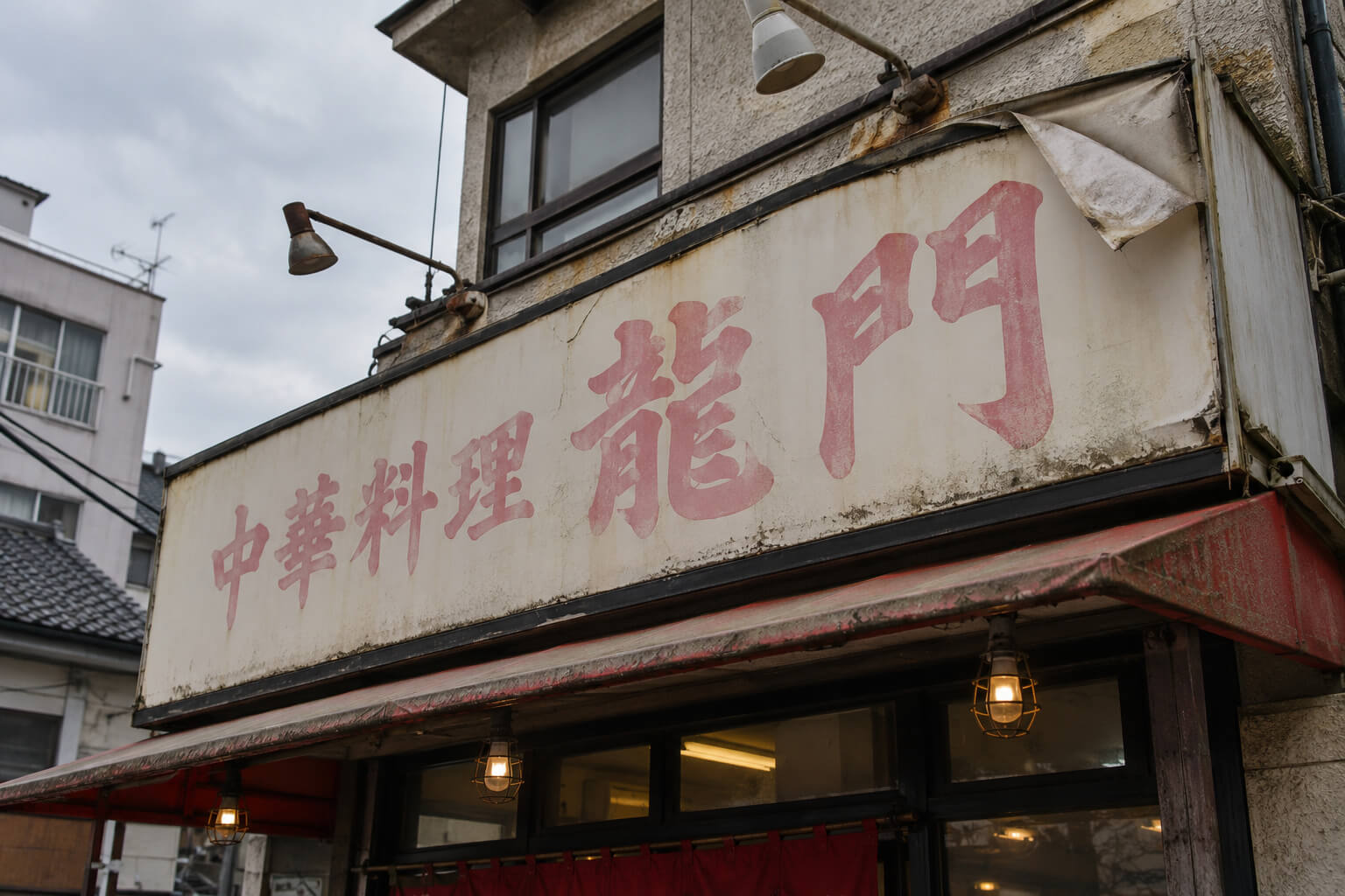 日焼けで赤い文字が薄いピンク色に色褪せ、シートの端が浮いている壁面看板