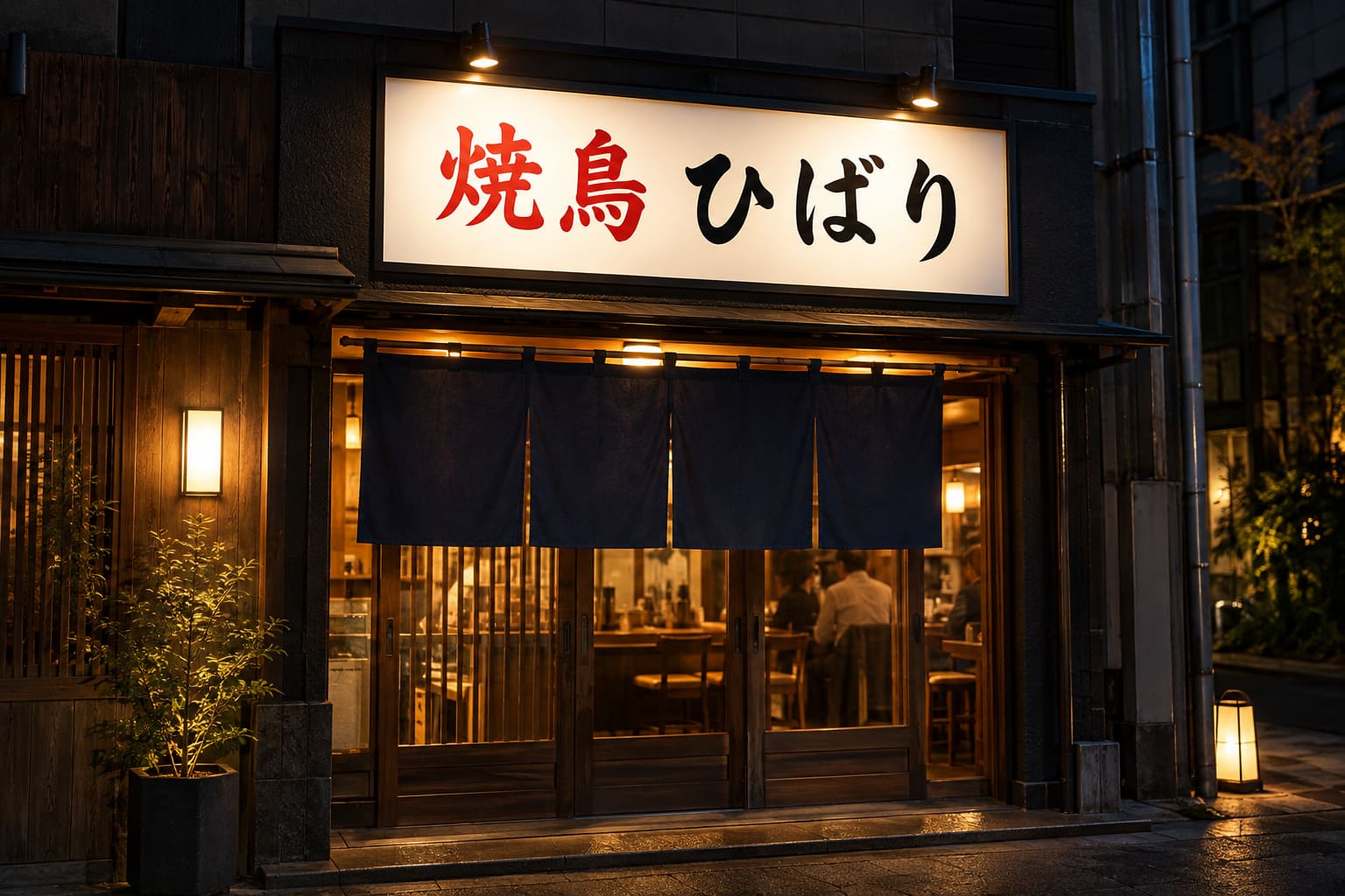 夜の焼き鳥店の入口の上の壁に、黒いアルミ枠の横長の看板が付き、上から小さなLEDのライトで照らされている様子