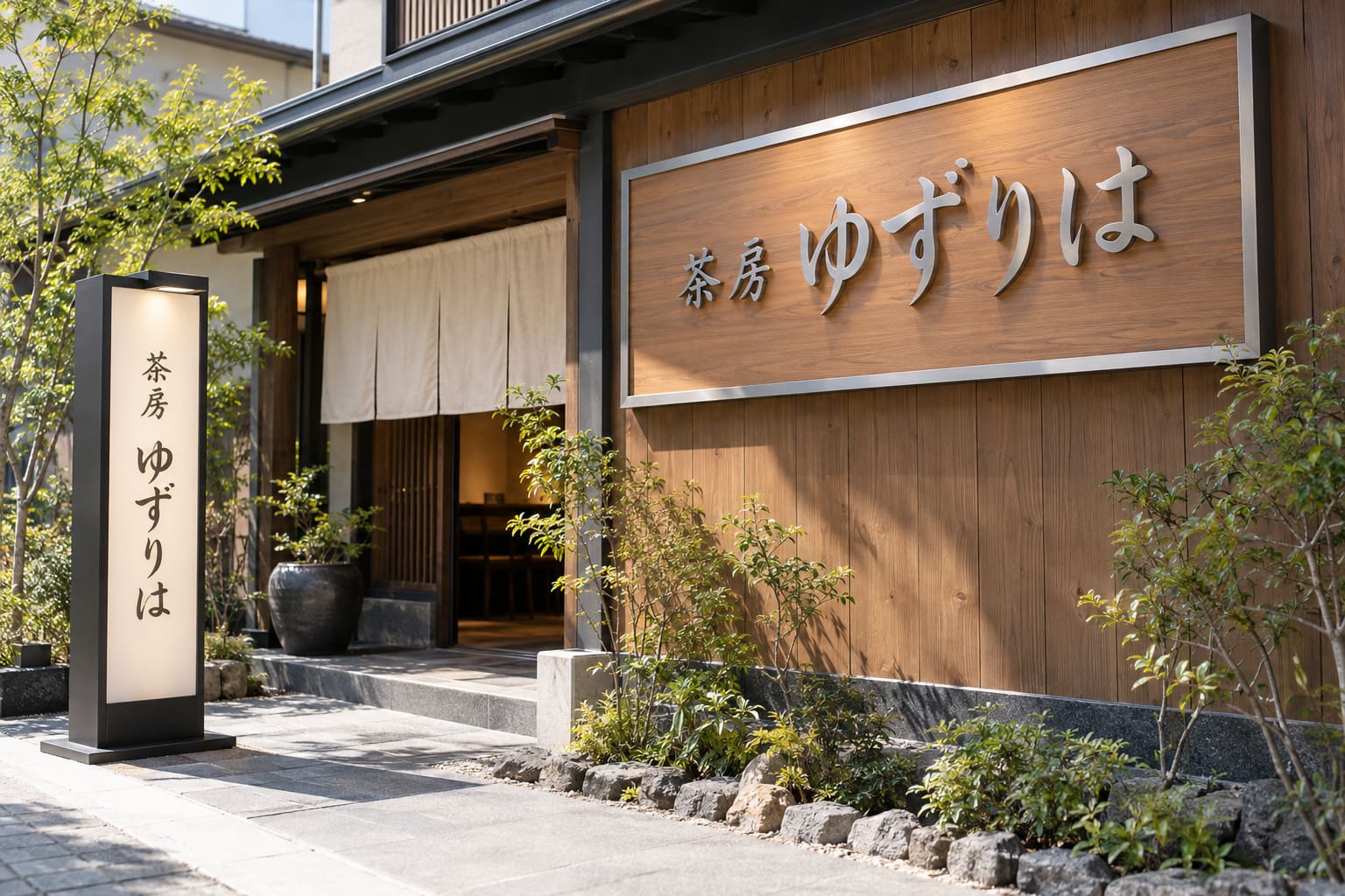 和風のカフェの外観で、木目の壁にアルミ枠の大きな看板とステンレスの箱文字が付き、入口の横に両面の自立看板が立っている様子