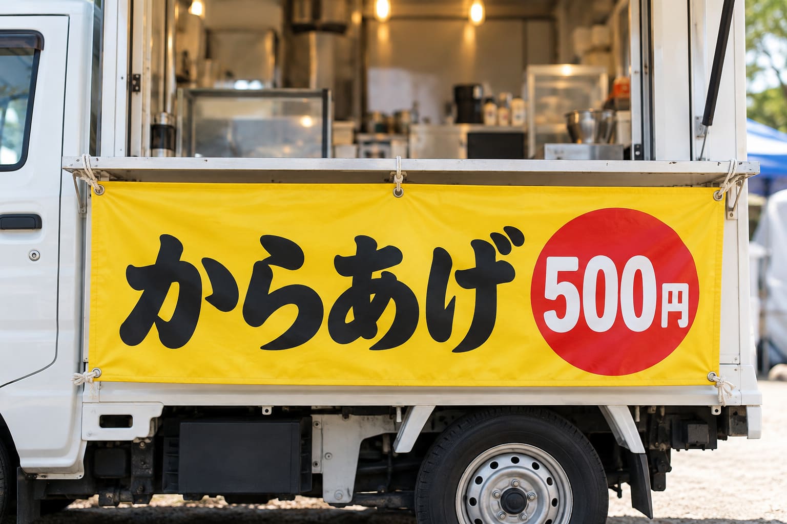 黄色い横長の幕に「からあげ」の文字と値段を大きく入れ、キッチンカーの販売窓の下に張った様子