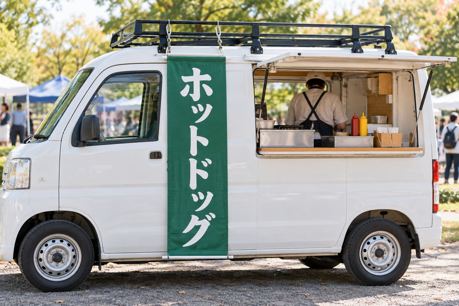 キッチンカーの屋根のルーフキャリアの横の棒から、カラビナでタペストリーを吊るしている様子