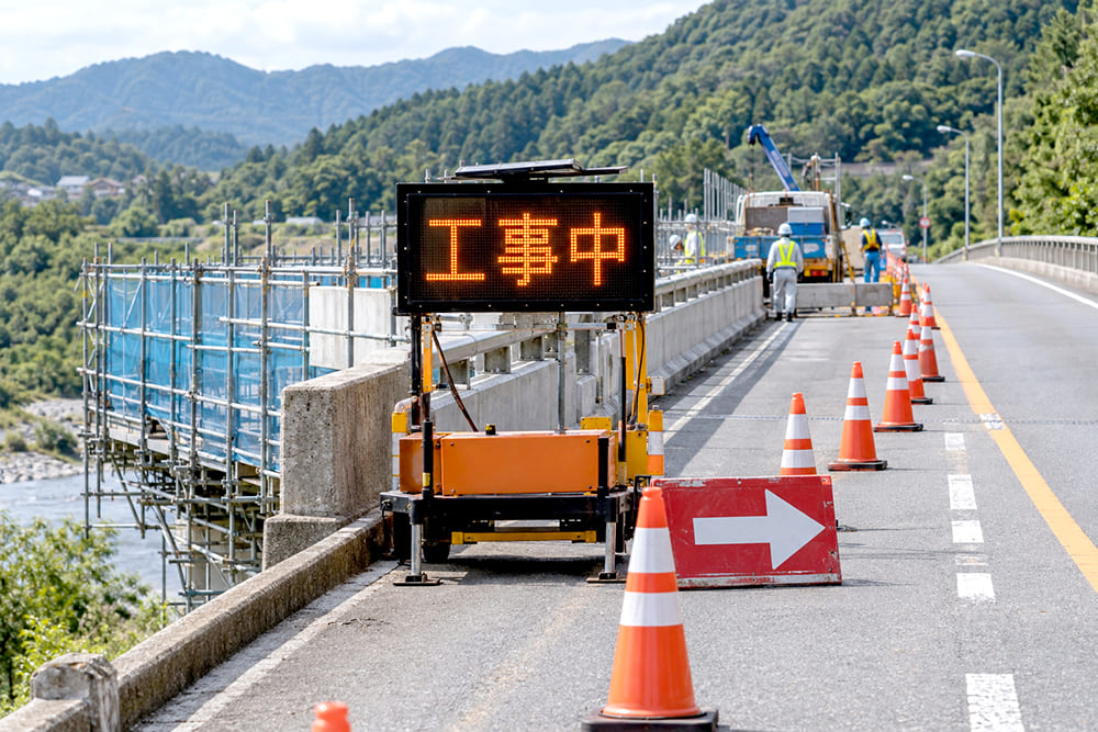 橋の上で片側の車線を規制して補修工事をしていて、電光標示板と矢印板、コーンが並んでいる様子