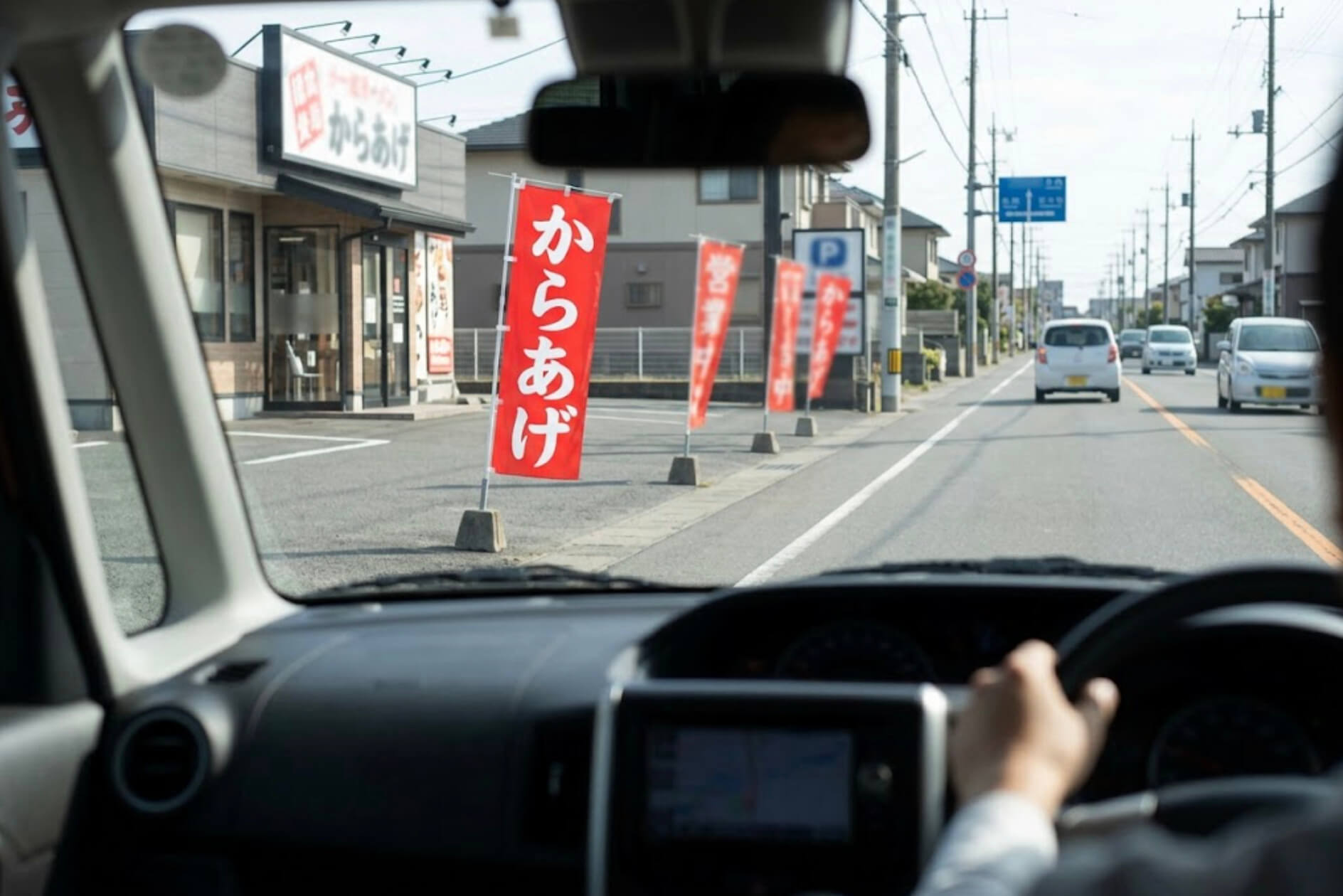 道路沿いの店の前に立つのぼり旗を、走っている車の運転席から見た様子