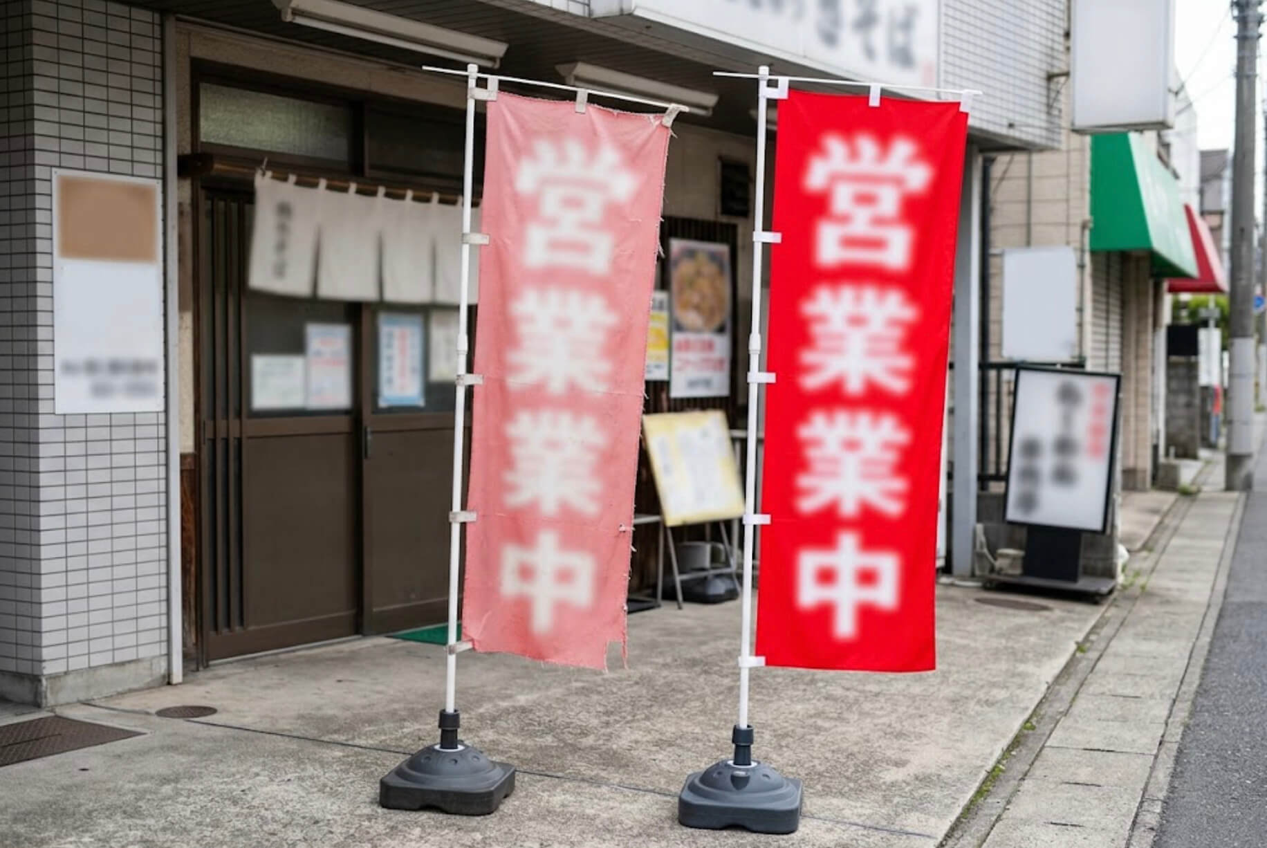 色あせて文字が薄くなったのぼり旗と、新しい鮮やかなのぼり旗が並んでいる様子