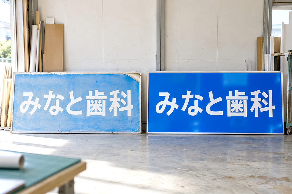 同じ形の2枚のプレート看板を並べ、左は日焼けで色があせてシートの端がめくれ、右は表面のシートを貼り替えて色が鮮やかに戻っている様子