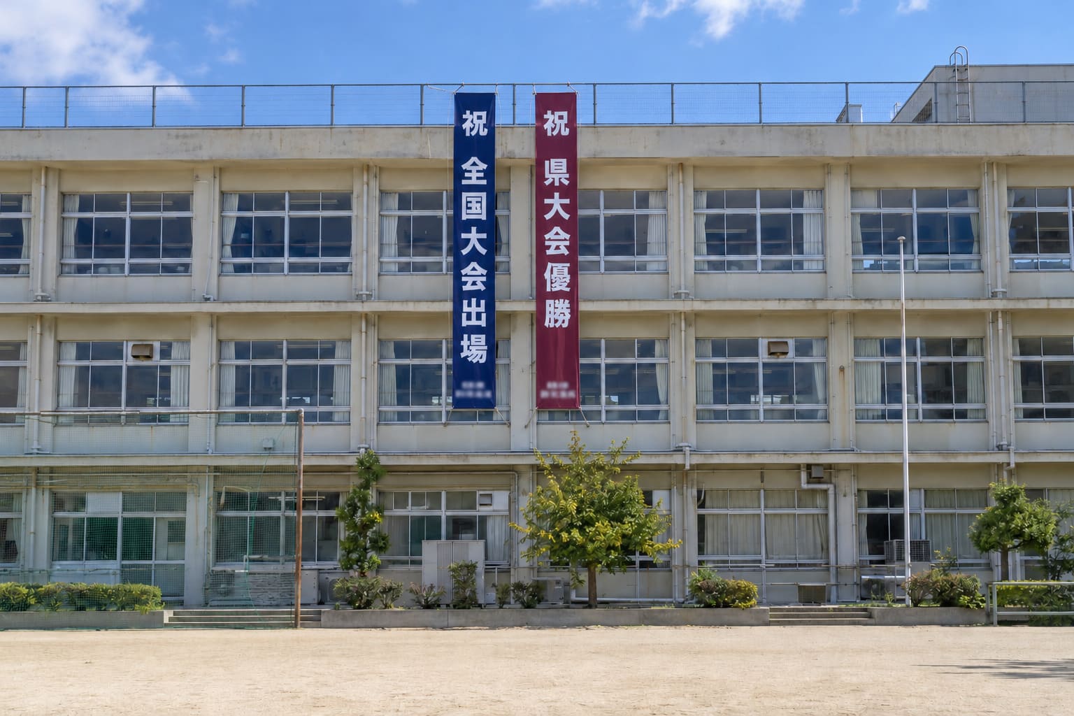 3階建ての校舎の屋上から、部活動の大会出場を知らせる縦長の垂れ幕が2本下がっている様子