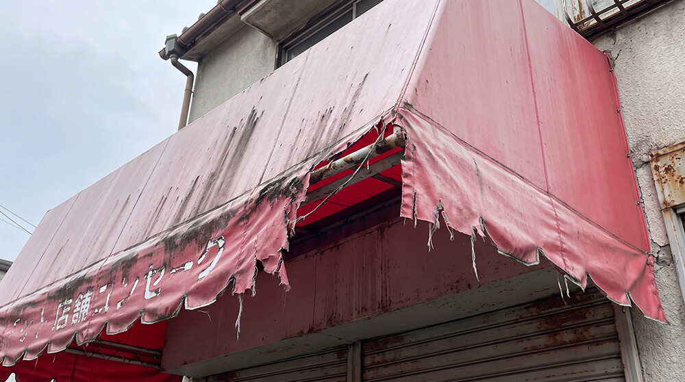 色あせて端が破れ、文字がかすれた古い店舗テントを、近くから見上げた写真